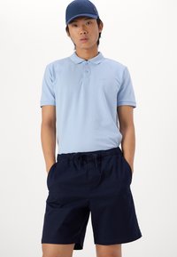 Polo bleu clair avec un col et trois boutons, associé à un short marine avec une taille élastique et des poches latérales.