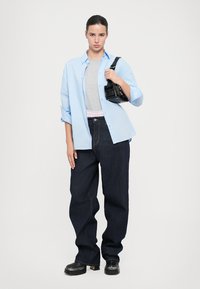 Svetlo modra srajca s kravatami čez sivo majico, v kombinaciji s temno modrimi širokimi jeans hlačami. Drži majhno črno torbico.