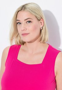 Top senza maniche fucsia con scollatura quadrata, dalla texture liscia, dotato di spalline dritte. Il modello ha capelli biondi corti e orecchini a cerchio.