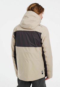 Beige en zwarte waterdichte jas met een capuchon, met een kleurblok ontwerp, een gladde textuur en een logo op de schouder.