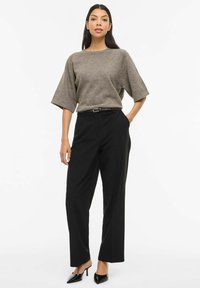 Pelēks pārizmēra džemperis, melnas augsta vidukļa bikses un melnas augstpapēžu kurpes ar smailu purngalu. Minimālistisks dizains ar gludu tekstūru bez rakstiem.