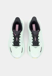 Scarpe da corsa verde chiaro con tomaia testurizzata, lacci neri e accenti rosa, dotate di una suola ammortizzata e design in mesh traspirante.