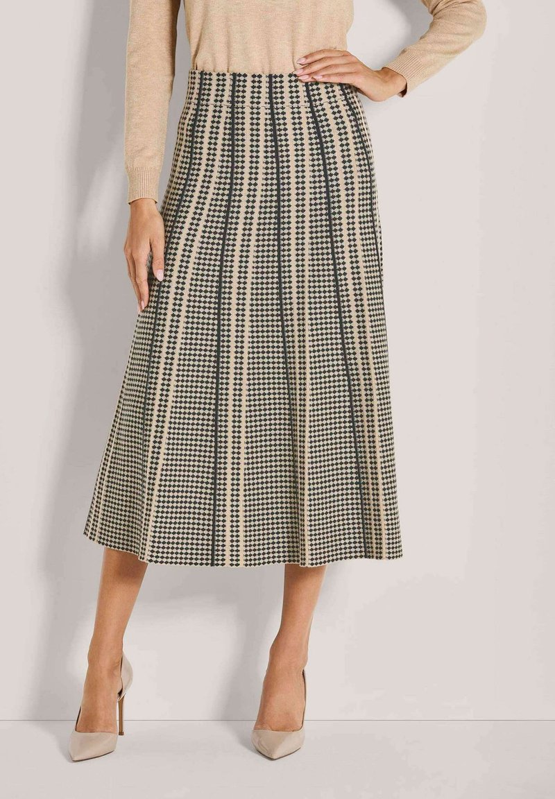 Beige und schwarze kariert midi Rock, getragen mit beigem Langarmoberteil und beigen High-Heels, Modell steht mit einer Hand auf der Hüfte.