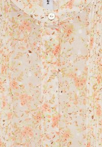 Bloemige blouse met knopen in lichtgewicht, doorzichtig materiaal met een crèmewitte achtergrond en perzik- en groene bloemenpatronen en textuur.