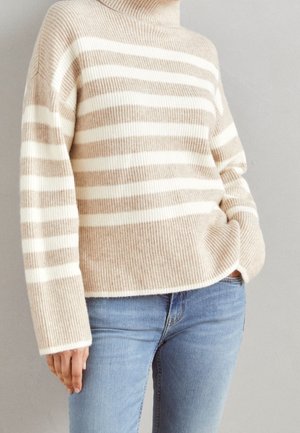 Beige-wit gestreepte coltrui met geribbelde brei, gecombineerd met lichtblauwe spijkerbroek, gedragen door persoon met hand in zak.