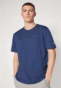 Navyblaue Baumwoll-T-Shirt mit Rundhalsausschnitt und gesticktem, kontrastierendem "Champion"-Logo. Kurze Ärmel und lockere Passform.