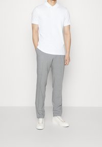 Vitt polotröja med krage, ihop med ljusgrå, texturerade byxor. Vita sneakers med färgglada snören fulländar outfiten.