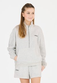 Hellgrauer Reißverschluss-Hoodie mit hohem Kragen und Fronttasche, kombiniert mit passenden Shorts, die schwarze Marken-Textakzente aufweisen.