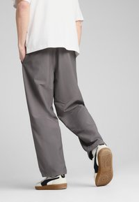 Pantalones grises, holgados y con una textura suave. Combinados con zapatillas blancas y negras con suelas de goma. Estilo casual, diseño discreto.