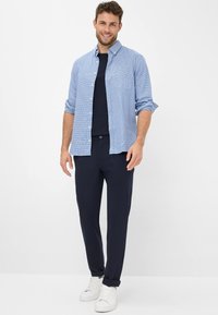 Blauw-wit geruit overhemd met knopen over een marineblauw T-shirt, gecombineerd met marineblauwe broek en witte sneakers. Casual pasvorm met opgevouwen mouwen.