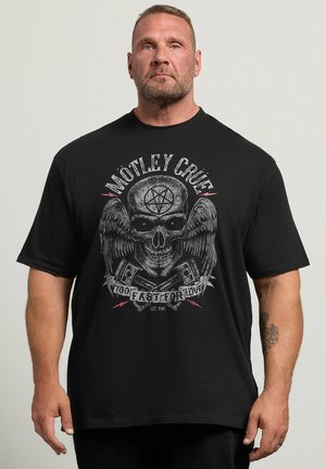 Homme aux cheveux courts et à la barbe portant un t-shirt noir Motley Crue arborant un design de crâne ailé et de pistons croisés.