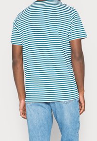 Camiseta de manga corta a rayas azul y blanca con cuello redondo y corte holgado, combinada con jeans de mezclilla azul claro.