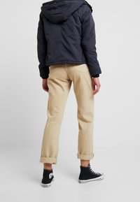 Sort oppustet jakke med hætte, beige oprullede chinos og sorte høj-top sneakers. Funktioner inkluderer en tekstureret overflade og afslappet pasform.