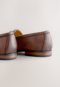 Paire de chaussures habillées marron en cuir à enfiler avec surface texturée et semelles superposées noires et marron sur fond clair.