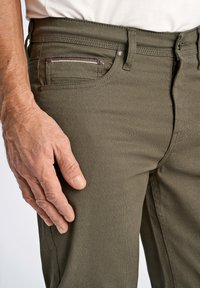 Pantalons texturés vert olive avec une fermeture éclair et un bouton, dotés d'une poche avant avec des accents de couture multicolores.
