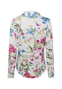Witte langwerpige blouse met een bloemig patroon in blauwe, roze en groene tinten. Zachte stof, knoopdetail op de mouwen, afgeronde zoom.