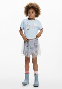 Blå cropped t-shirt med dyregrafik, grå tylnederdel med farverige mønstre og blå gummistøvler med lyserøde tie-dye sokker.