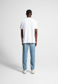 Vit t-shirt med rund halsringning och korta ärmar, kombinerad med ljusblå denimjeans. Jeansen har en avslappnad passform och slitna detaljer.