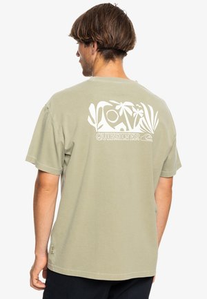 Camiseta de algodón verde olivo con un gran gráfico blanco en la parte posterior que presenta elementos tropicales y el nombre de la marca "Quiksilver" debajo.