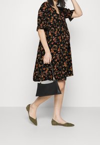 Schwarzes Blumenkleid mit kurzen Ärmeln, knielangem Saum, kombiniert mit olivgrünen Ballerinas und einer schwarzen strukturierten Handtasche.