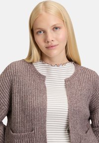 Gruby, pleciony kardigan w miękkim odcieniu mauve, z prążkowaną fakturą, z okrągłym dekoltem i dwiema przednimi kieszeniami. Paski na koszulce pod spodem.