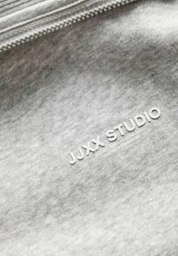 Tela gris con una textura sutil que presenta el nombre de la marca en relieve "JUXX STUDIO" en blanco, junto con texto adicional en una fuente más pequeña.