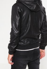 Zwarte leren jas met capuchon, met een getailleerd ontwerp, geribbelde boorden en een gladde textuur. Van achteren getoond, met accent op de naaddetails.