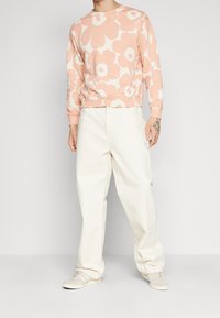 Felpa rosa chiaro con grande motivo floreale bianco, scollo a girocollo, polsini a costine, abbinata a pantaloni a palazzo color crema e sneakers chiare.