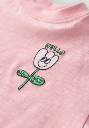 Rosa Baumwoll-T-Shirt mit sticktem Blumenmotiv, das ein lächelndes Gesicht zeigt, darüber der Schriftzug "HELLO" und auf einem grünen Blatt der Schriftzug "NEW DAY".