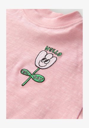 Roosa puuvillane t-särk, millel on tikitud lillekujundus naeratava näoga, üleval tekst "HELLO" ja rohelisel lehel tekst "NEW DAY".