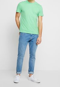 Camiseta de algodón verde de manga corta, combinada con unos vaqueros de mezclilla azul claro arremangados en los puños y zapatillas blancas. Diseño simple.