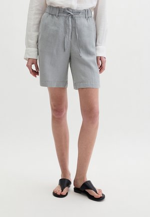 Hellgraue knielange Shorts mit gebundenem Taillenband, getragen zu einem weißen Langarmhemd und schwarzen Sandalen mit offenen Zehen.