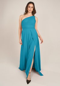 Ein einseitiger, bodenlanger Abendkleid in lebhaftem Teal, mit drapiertem Stoff und einem schlitz bis zum Oberschenkel, aus glattem, leichtem Material.