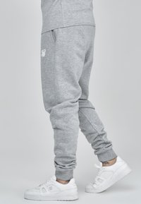 Gray sweatpants with a soft texture and elastic cuffs, featuring side pockets and a white embroidered logo. Paired with white sneakers.