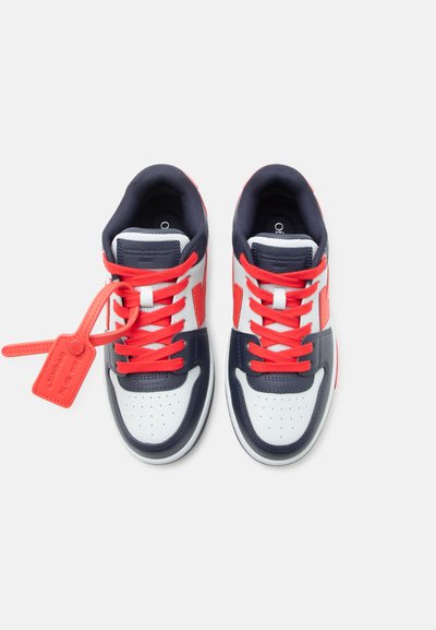 Een paar witte, marineblauwe en rode sneakers met rode veters en een rood label bevestigd aan de linkerschoen, gezien van bovenaf op een witte achtergrond.