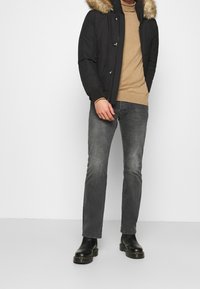 Schwarze Daunenjacke mit fellgefütterter Kapuze, beiges Sweatshirt, graue Jeans und schwarze Stiefeletten mit klobigen Sohlen. Einfaches, modernes Design.