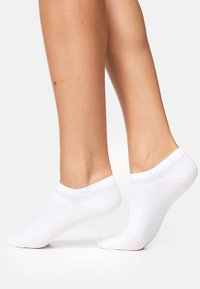 Calzini bianchi alla caviglia realizzati in tessuto morbido con design a taglio basso. Presentano un motivo a zigzag nel risvolto, garantendo una vestibilità sicura.