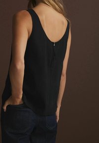 Top senza maniche nero con scollo profondo, caratterizzato da una chiusura con cerniera discreta. Il tessuto ha una texture liscia, abbinato a jeans di denim scuri.
