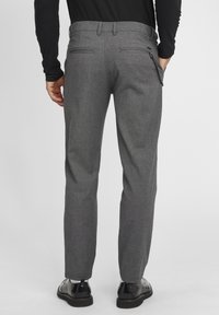 Sive hlače u herringbone uzorku, slim fit, sa bočnim džepovima i suptilnom teksturom, uparene s crnim kožnim cipelama.