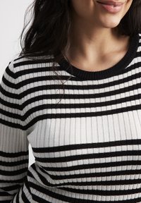 Black and white striped ribbed sweater with a round neckline and textured fabric. Horizontal stripes vary in width across the garment.