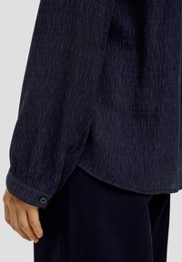 Mörkblå texturerad skjorta med en strukturerad design, som har en knappad manschett och en svagt böjd fåll. Mjuk tyg med ett subtilt mönster.