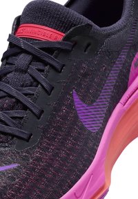 A Nike Invincible Run cipők sötétlila, texturált kötött felsőrésszel rendelkeznek, rózsaszín díszítésekkel és párnázott talppal, amelyen lila swoosh logó található.