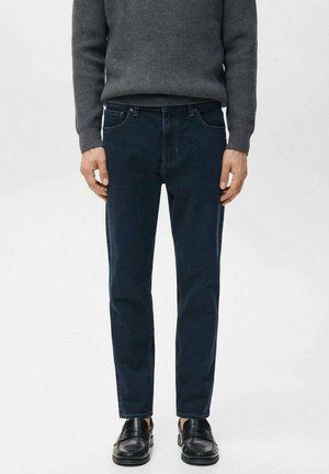 Pantalones vaqueros de mezclilla azul oscuro con un corte ceñido. Combinados con un suéter de punto gris y mocasines negros. Presentan bolsillos clásicos y un diseño limpio.