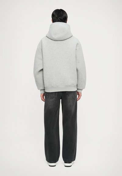 Haut de survêtement gris surdimensionné avec une grande capuche, vu de dos, assorti à un jean gris foncé ample et des baskets blanches.