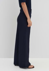 Wijdvallende broek in marineblauwe stof. Heeft een hoge taille, een gladde textuur en zijzakken. Gestyled met platte sandalen.