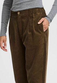 Brown corduroy pants with pleats, a button closure, and side pockets. The texture is ribbed, and the waistband includes elastic for comfort.
