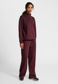 Burgundy zip-neck tröja med framficka, matchad med vida byxor. Premiumtyg med mjuk textur; sportskor med flerfärgade detaljer.