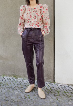 Blumenbluse mit Rüschendetails und Knöpfen, kombiniert mit hochgeschnittenen lila Lederhosen und beigen geflochtenen Slippern. Texturierte Details sichtbar.