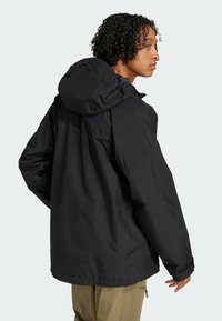 Sort vandtæt jakke med hætte, i en løs pasform, elastiske manchetter og en snøret kant. Stoffet har en glat, mat tekstur.
