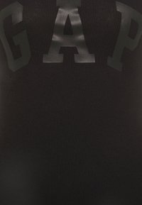 Svart ribbad linne med stora mattsvarta "GAP" bokstäver på framsidan, med en figurnära design och mjuk textur.
